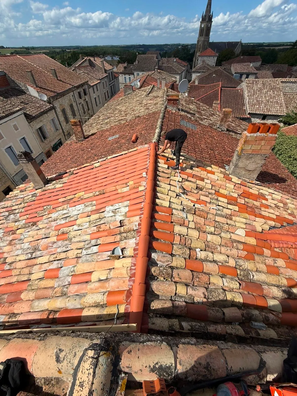 Couvreur rénovant un faîtage en tuile canal dans un village du Gers